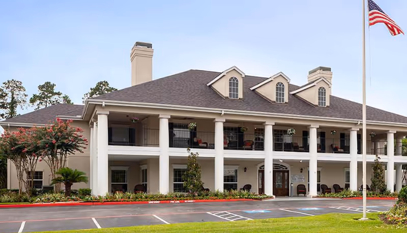 Exterior view of Novellus Cypresswood senior living facility with white columns and flag.