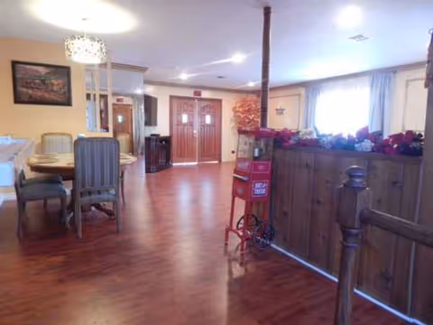 Interior common area of a senior living facility with dining table, chairs, and a flower-adorned railing.