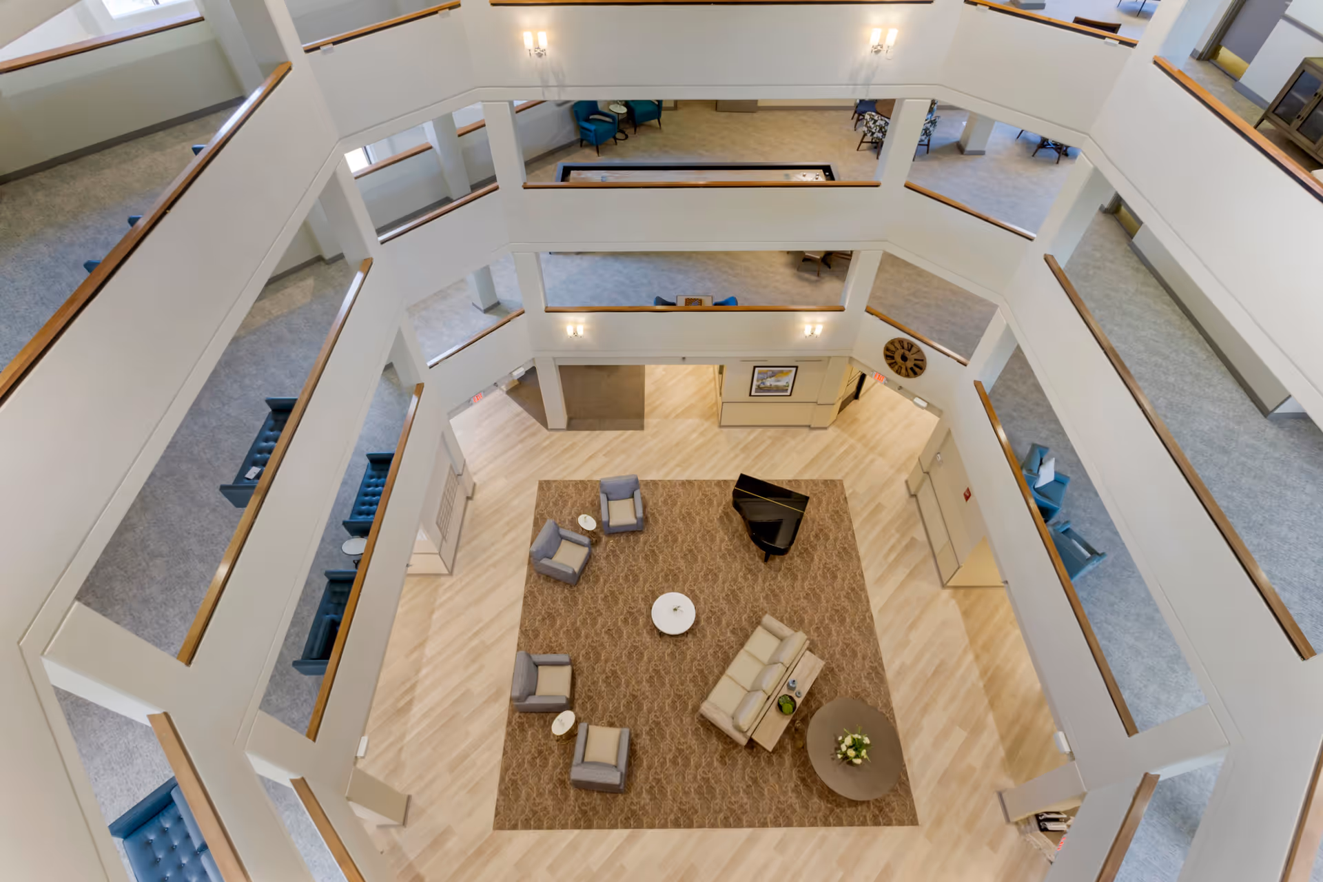 Multi-story atrium interior with a central seating area, a grand piano, and surrounding balcony walkways.
