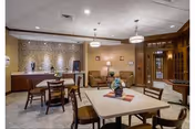 Communal dining area with square tables and chairs, pendant lights, a patterned accent wall, and a small seating nook with sofas.
