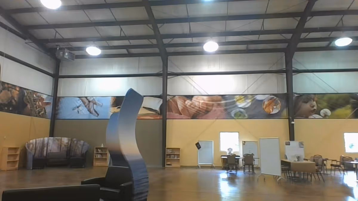 Large open interior room with high exposed-beam ceiling, scattered tables and chairs, and a curved decorative partition.