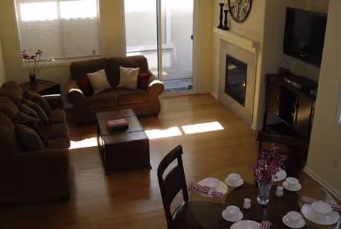 Cozy living room with brown sofas, fireplace, TV, and a dining table set near windows.