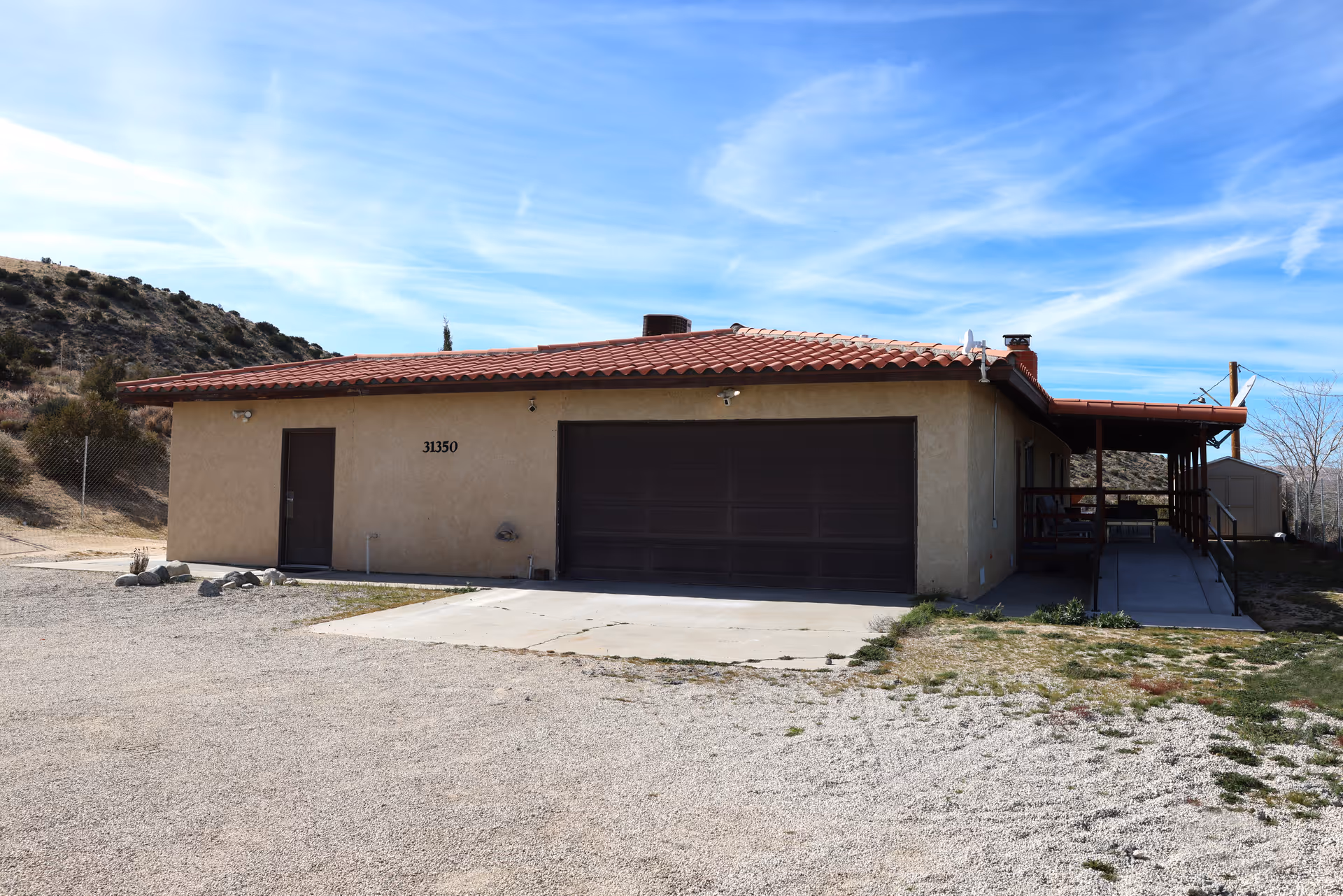 Single-story stucco building with a red tile roof and large garage door under a blue sky.