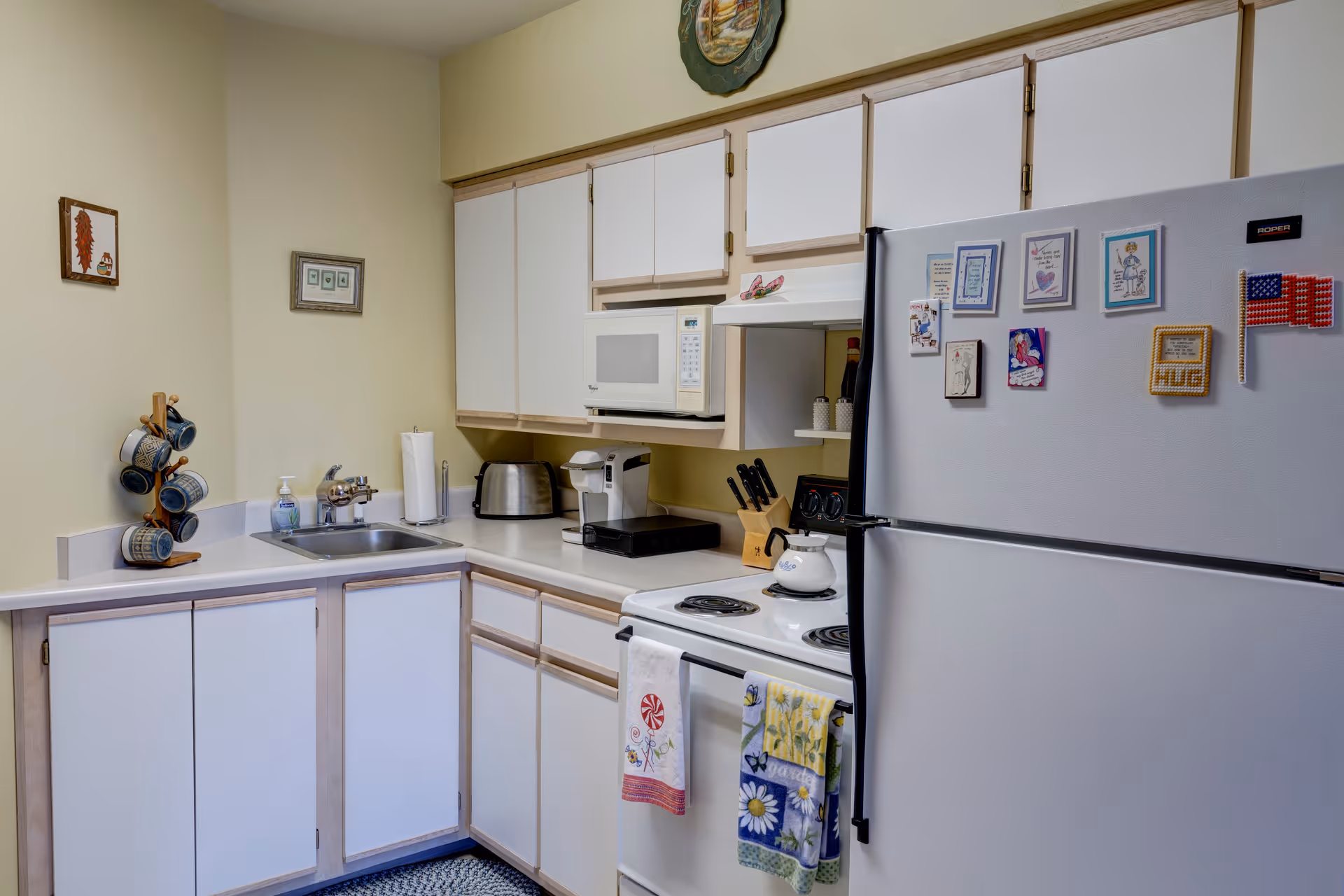 Compact kitchen with white cabinets, a microwave, stove, sink, and a refrigerator covered in magnets.