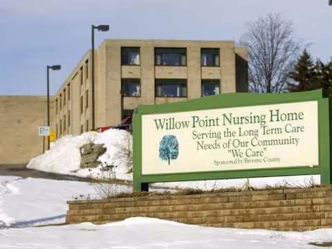 Exterior view of Willow Point Nursing Home with a green sign and snow piles.