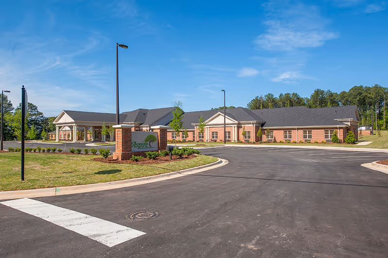 Front exterior of a single-story brick recovery center with a circular driveway, landscaped grounds, and a sign near the entrance under a blue sky.