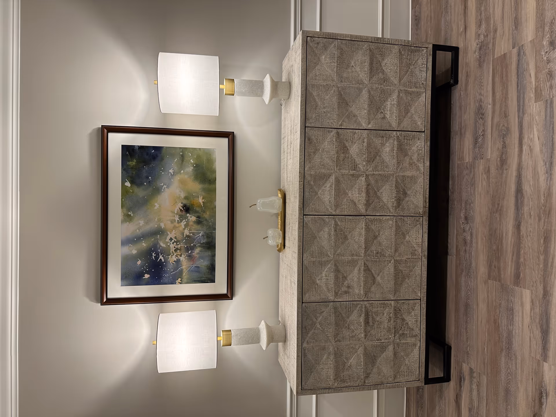 A patterned wooden console table with two table lamps beneath a framed abstract painting against an interior wall.