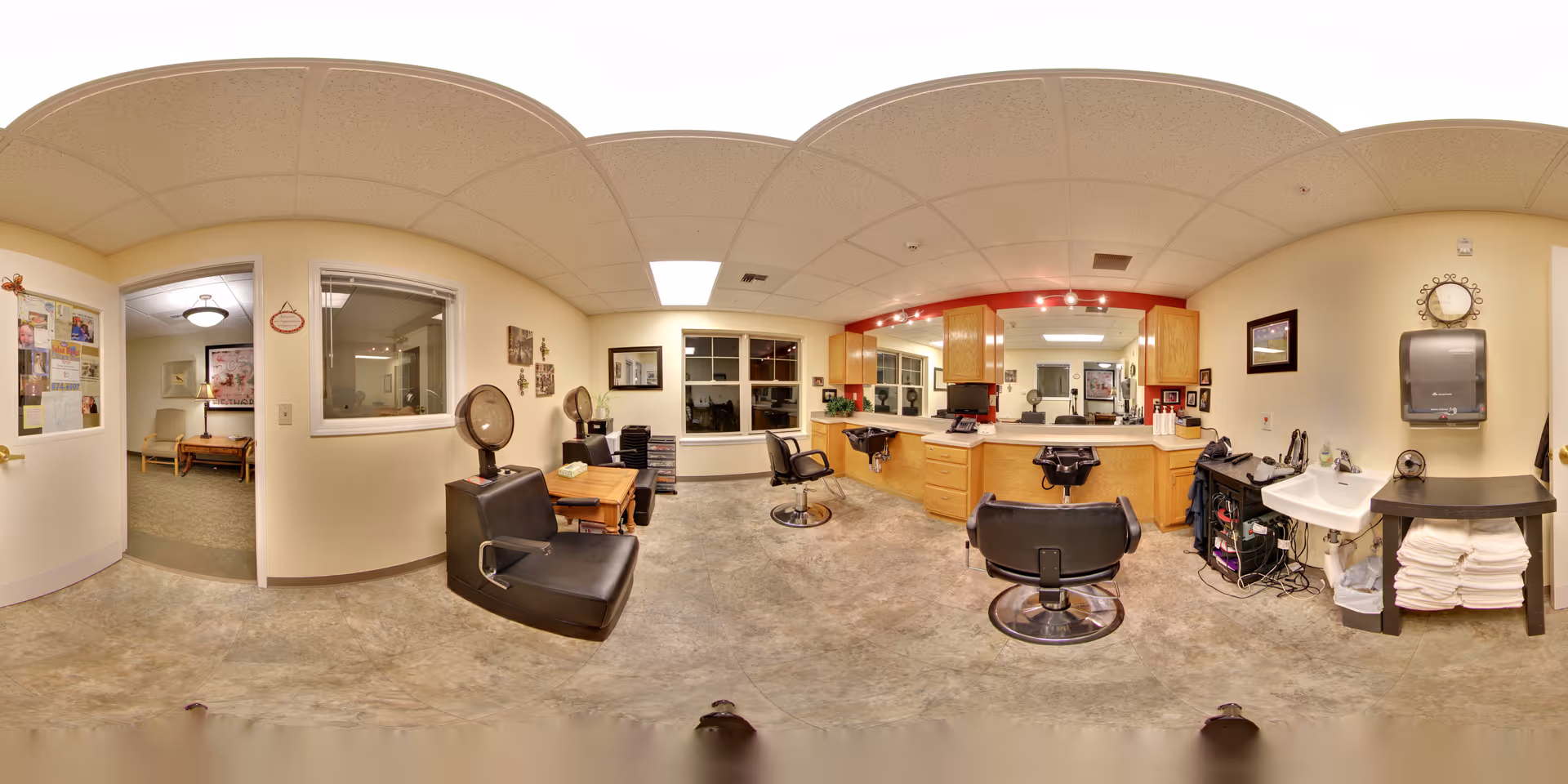 Panoramic interior view of a salon area in a senior living facility with styling chairs, mirrors, countertops, and a sink.