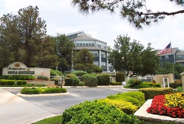 Landscaped entrance and facade of Independence Hill Retirement Community with a driveway, sign, and American flag.