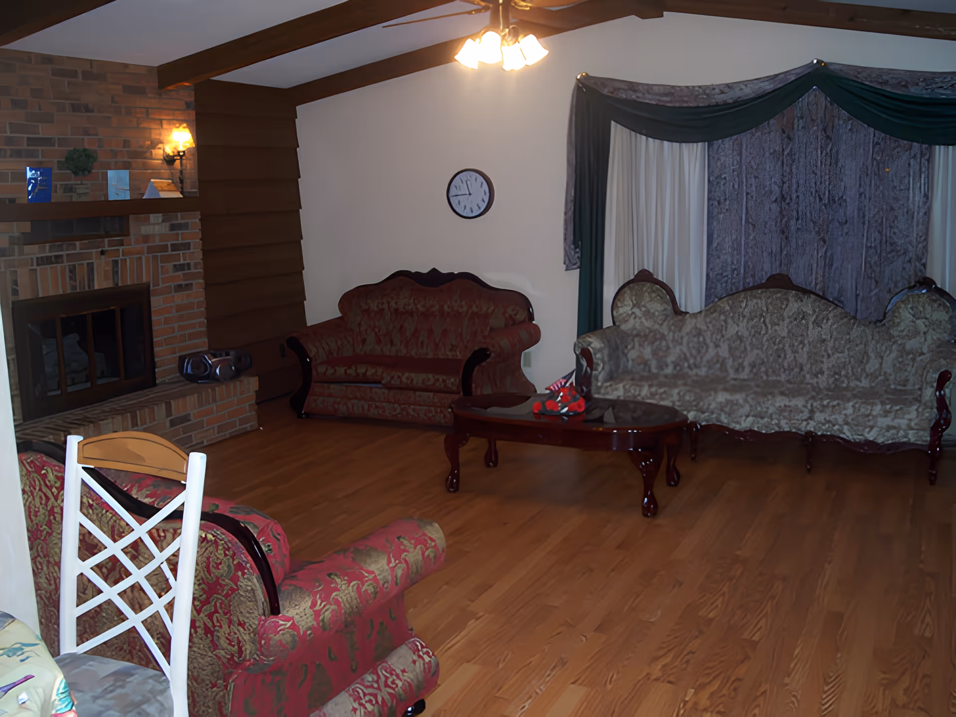 Spacious living room with vintage upholstered sofas, a wooden coffee table, brick fireplace and hardwood floors.