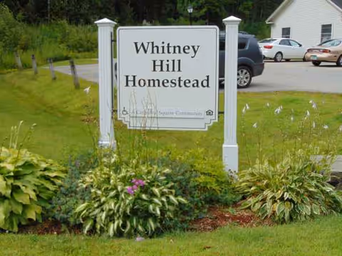 Whitney Hill Homestead sign in a landscaped front yard with parking in background