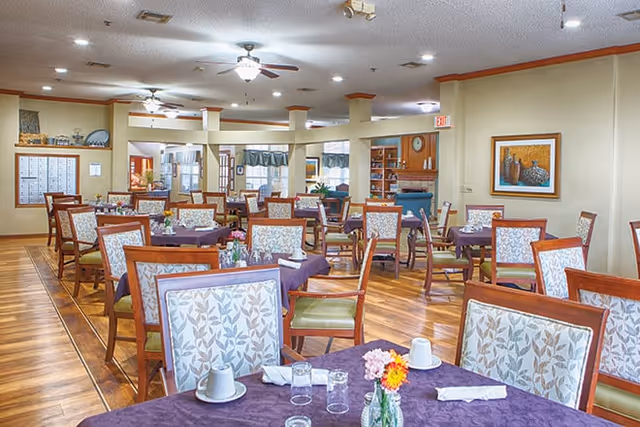 Dining room with multiple tables and chairs set with place settings and floral centerpieces.