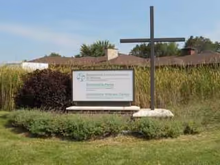 Outdoor view of Benedictine Living Community-Wausau sign with cross and shrub landscaping.