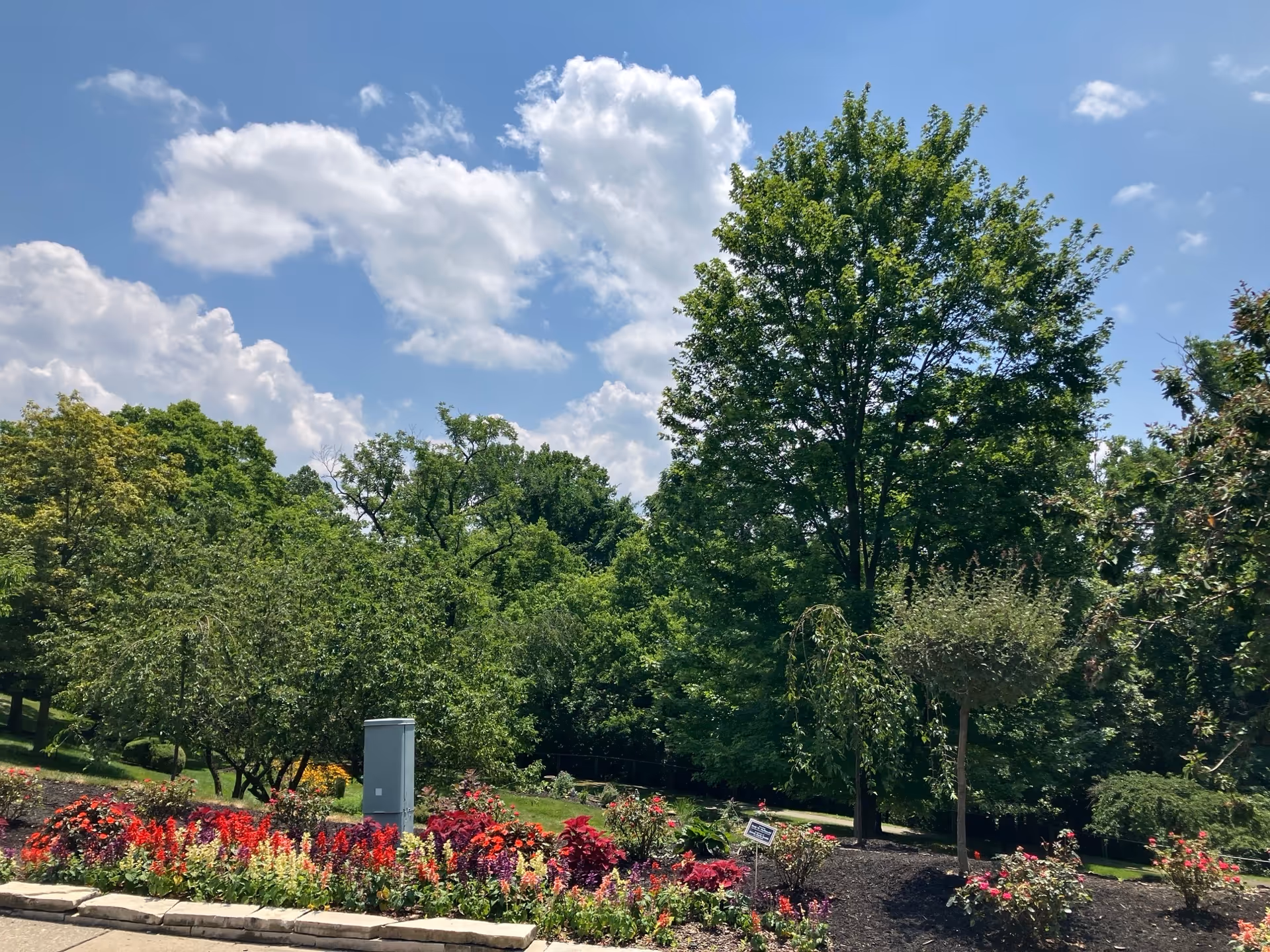 Colorful flower bed and landscaped grounds with trees beneath a blue sky with clouds.