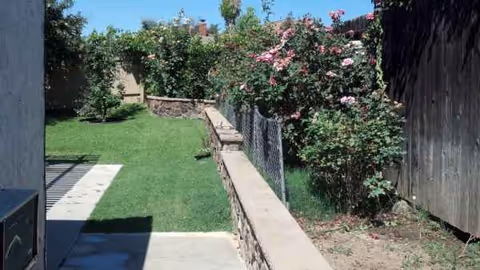 Outdoor side yard of Genesis Manor VI with grass, roses, and stone retaining wall