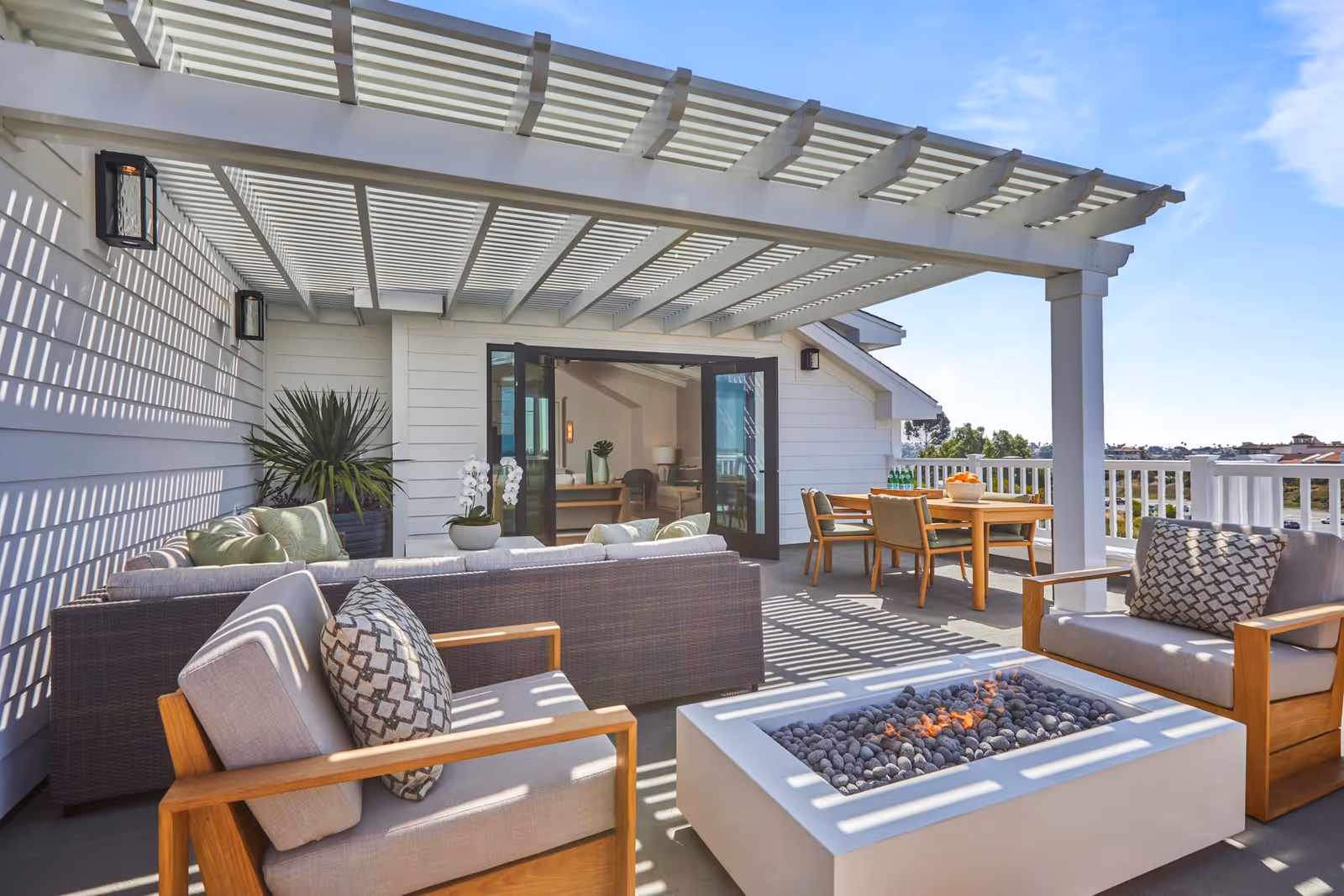 Sunny rooftop patio with cushioned seating, a fire pit, dining table, and pergola overlooking the neighborhood.