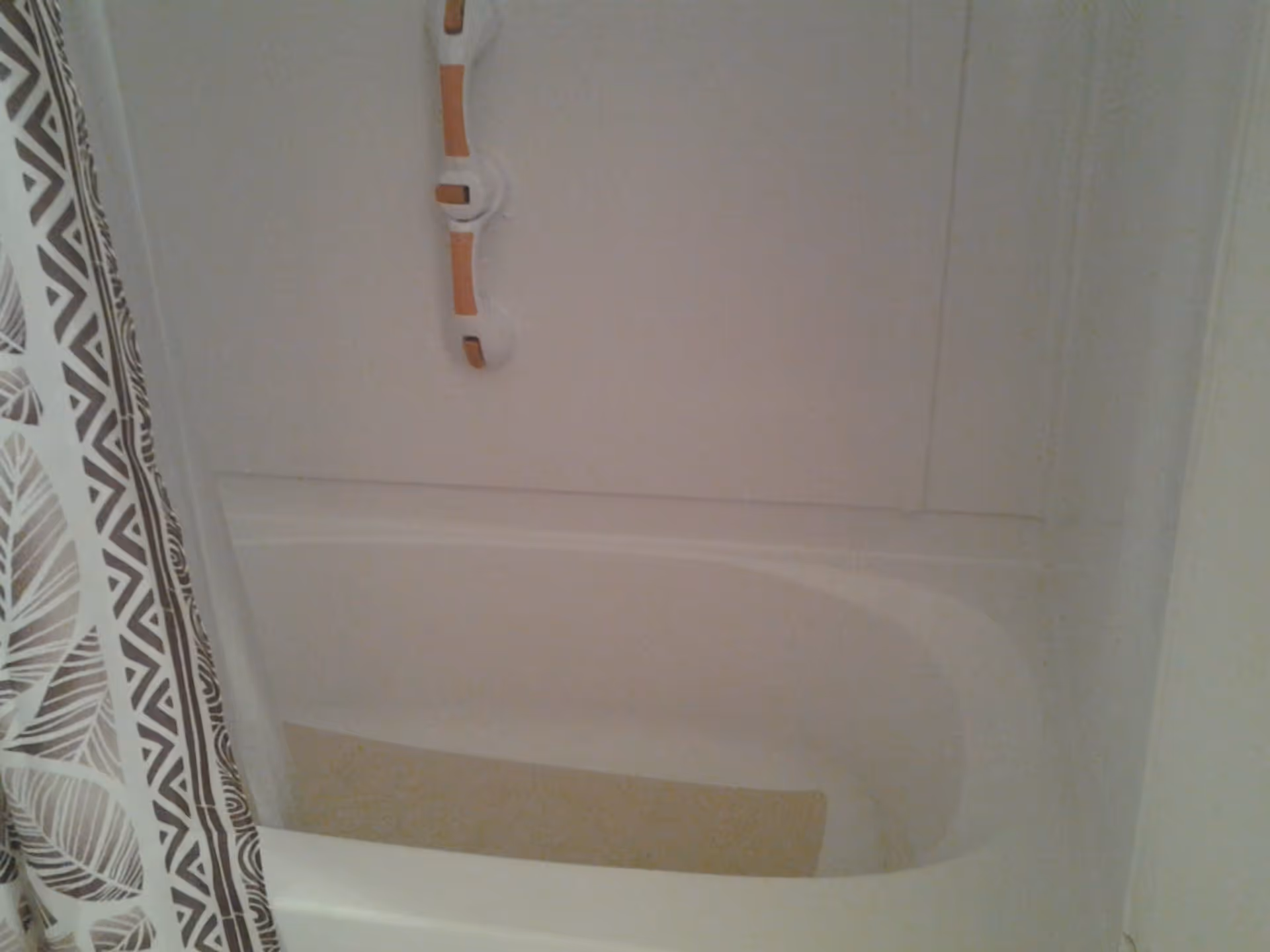 A white bathtub with a beige non-slip mat inside and a patterned shower curtain partially visible on the left side.