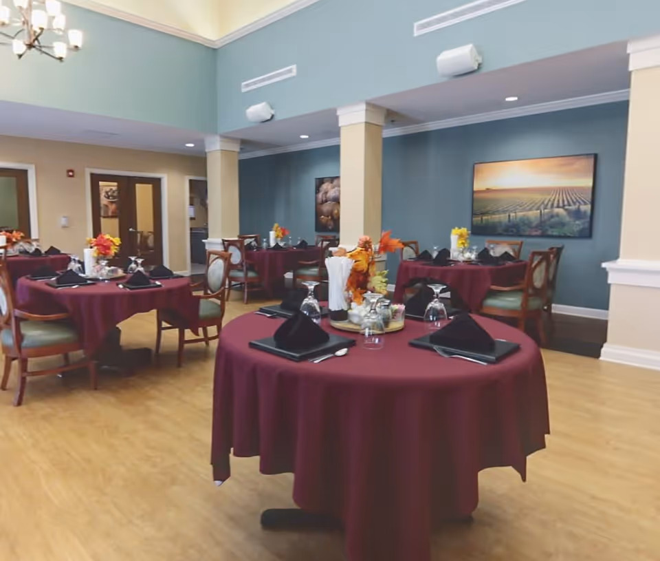 Dining room with round tables covered in burgundy tablecloths set with black napkins, glassware, and floral centerpieces.