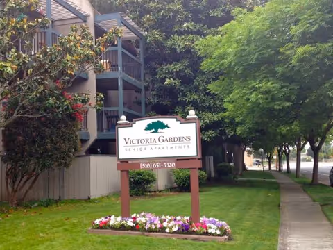 Exterior view of Victoria Gardens Senior Apartments with sign and landscaped lawn