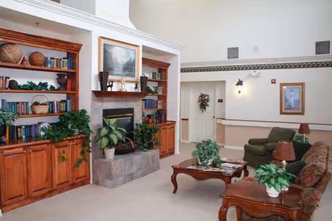 Cozy senior living room with fireplace, built-in shelves, plants, and comfortable seating.