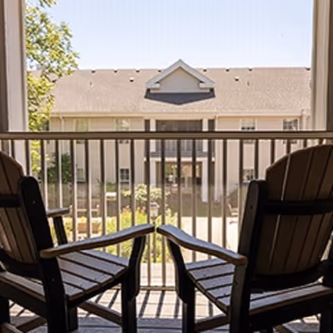 Two wooden chairs on a balcony overlooking a courtyard and an adjacent apartment building.