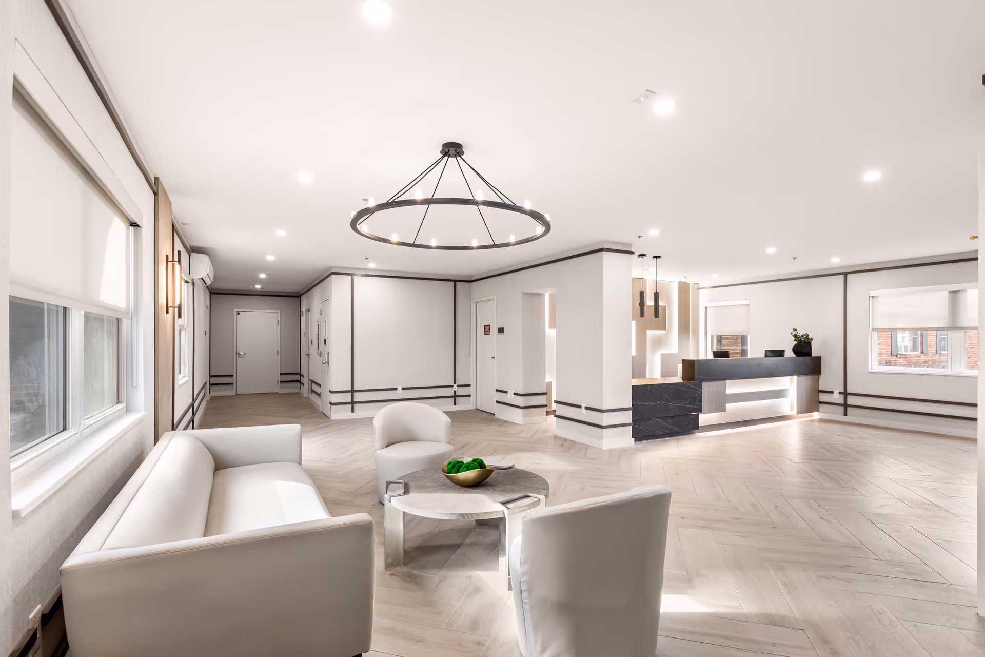 Bright modern lobby with a seating area of sofas and chairs, a round chandelier, and a reception desk.