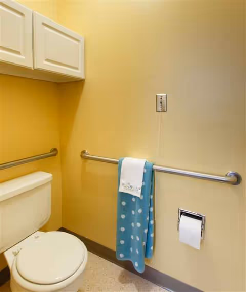 Yellow bathroom with a toilet, grab bars, towels, and cabinets.