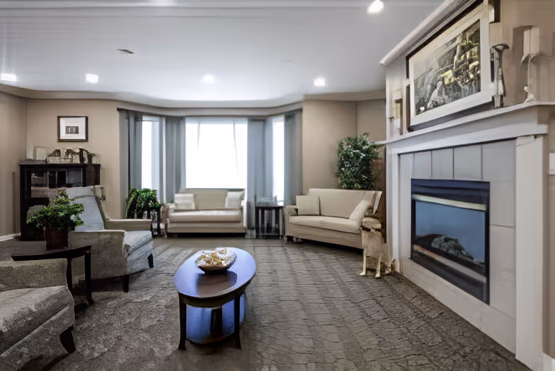 Spacious seating lounge with sofas and armchairs arranged around a central coffee table in front of a fireplace and bay window.