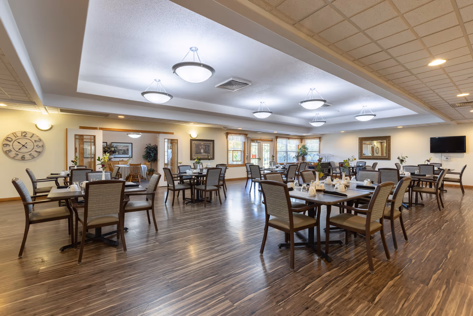 Spacious, well-lit dining room with multiple set tables and chairs and hardwood floors.