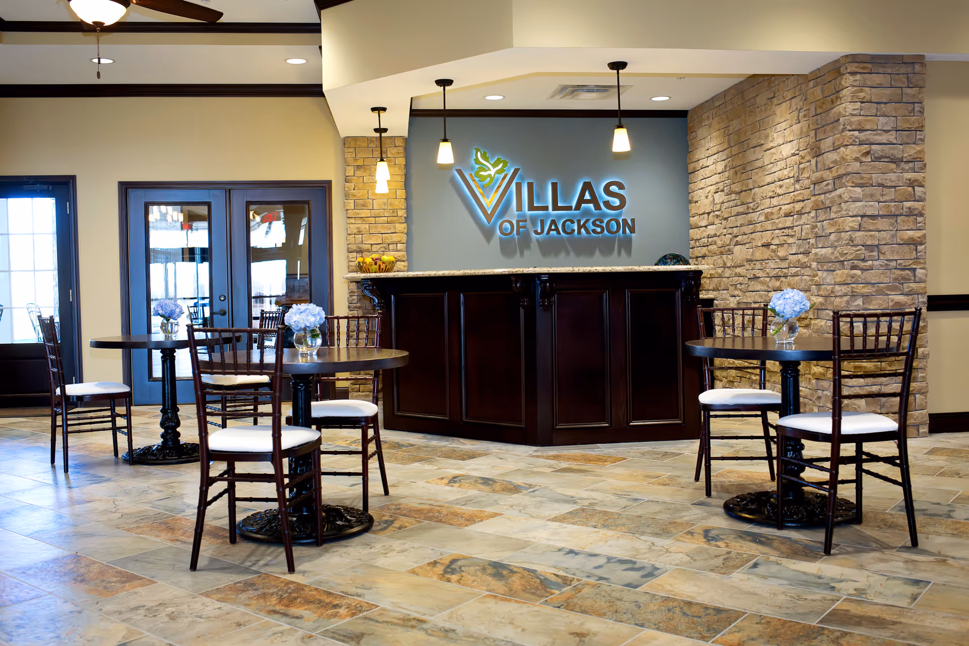 Lobby-style dining area with round tables and chairs in front of a reception desk bearing a 'Villas of Jackson' sign.
