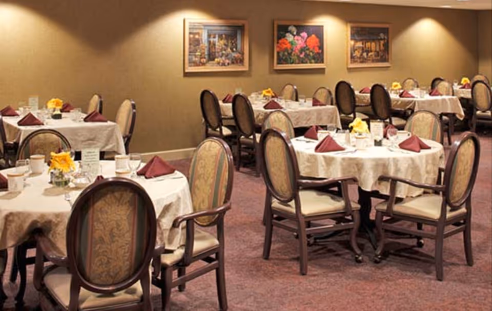 Dining room with round tables covered in white linens, place settings, folded burgundy napkins and yellow floral centerpieces.