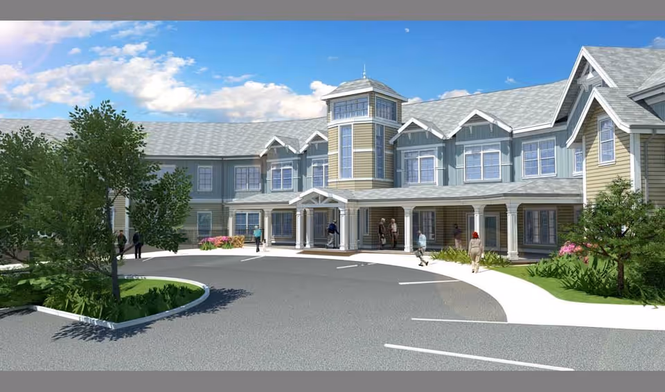 Exterior view of a senior living facility building with a circular driveway, landscaped greenery, and several people walking near the entrance under a clear blue sky.