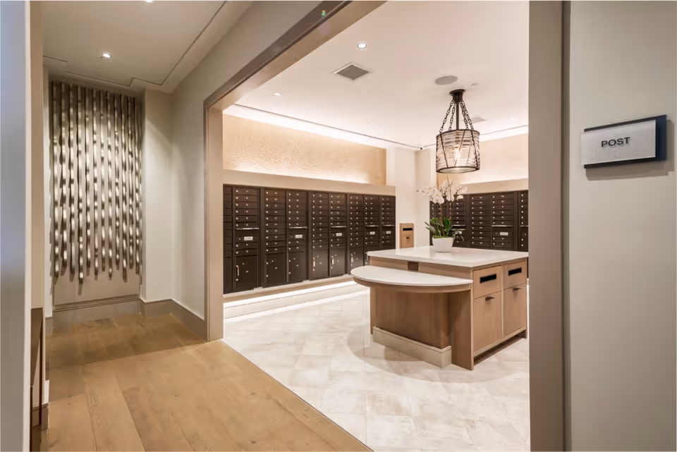 Interior mailroom with rows of wall mailboxes, a central wooden island, decorative lighting and a 'POST' sign on the wall.