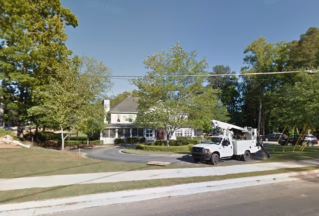 Front exterior of a two-story senior living building with a circular driveway, trees, and a utility truck parked in front.