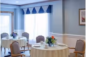 Sunlit dining room with round tables, white tablecloths, and blue-trimmed walls.