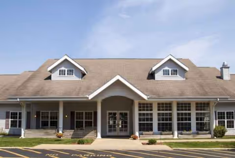 Front view of a single-story senior living facility with large windows and central entrance.