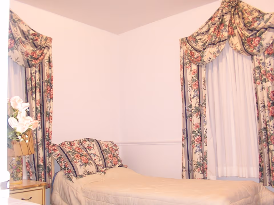 Small bedroom with a single bed, floral pillows and matching floral curtains and drapes.