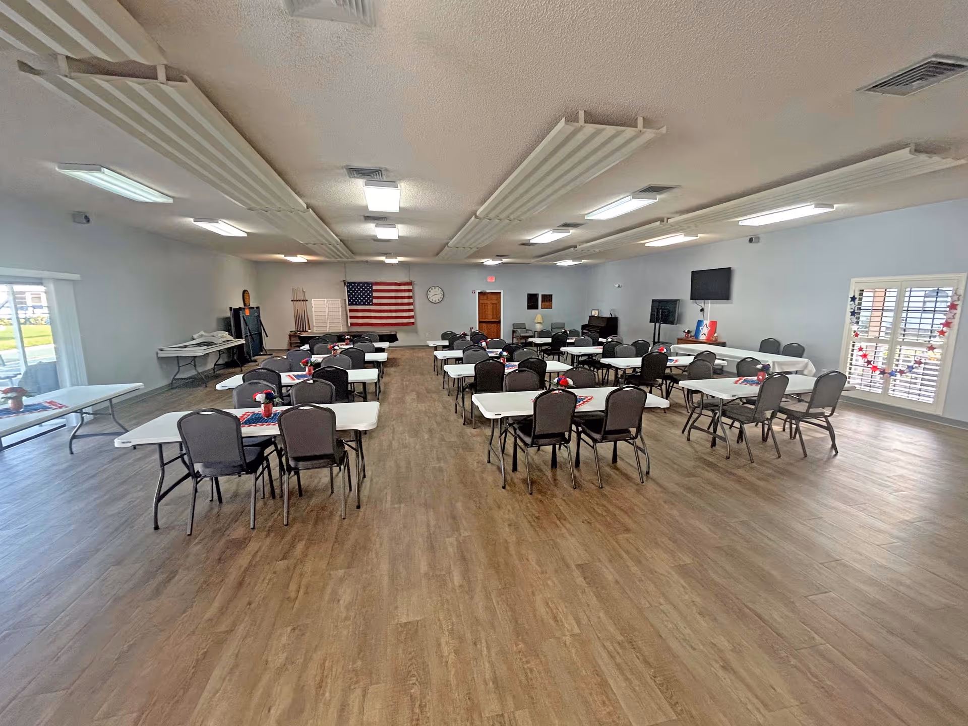 Large multipurpose dining/event room with rows of folding tables and chairs and an American flag on the far wall.