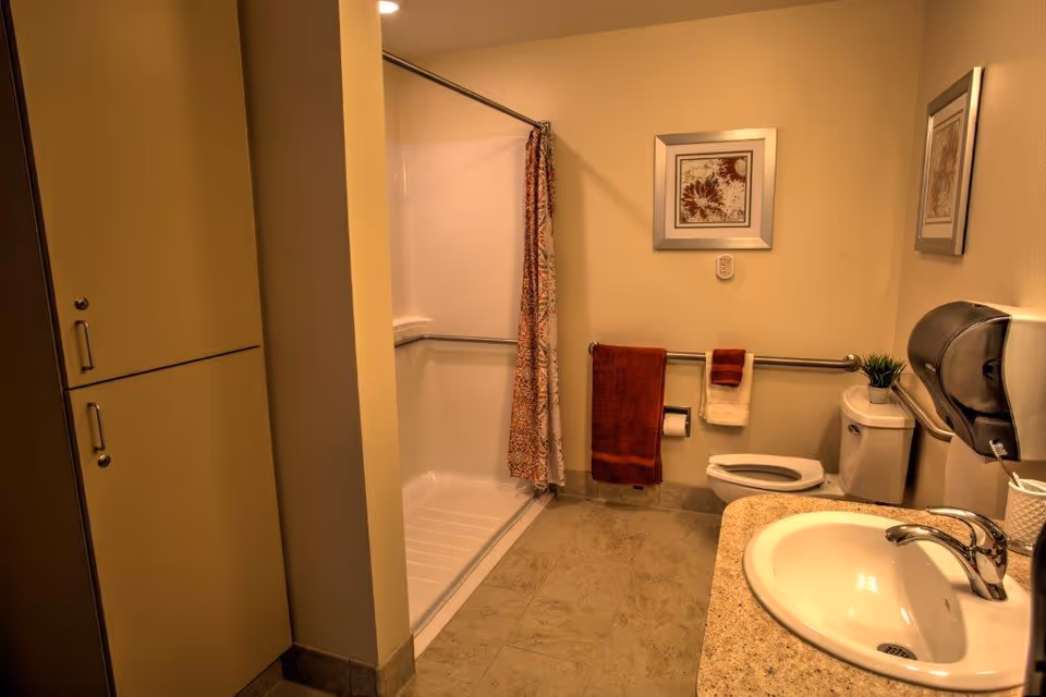 Accessible bathroom with a walk-in shower, toilet, sink, grab bars, and towels on a rail.