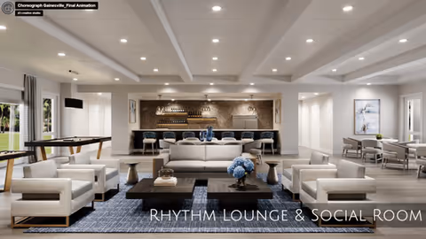 A spacious, modern lounge and social room with a white sofa, four white armchairs, two dark wooden coffee tables with decorative items, and a blue patterned rug. In the background, there is a bar area with stools and shelves holding bottles and glasses. To the right, there is a dining area with tables and chairs, and large windows letting in natural light.