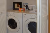 Front-loading washer and dryer in a closet with a laundry basket and detergent on top.