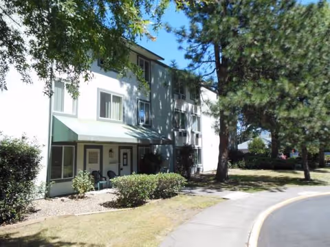 Two-story white retirement facility with green awnings, trees, and a curved walkway.