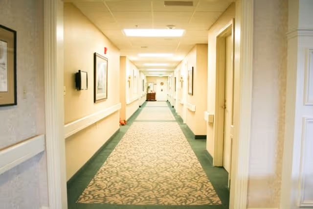 Well-lit, carpeted interior corridor with handrails, framed artwork, and doors on both sides.