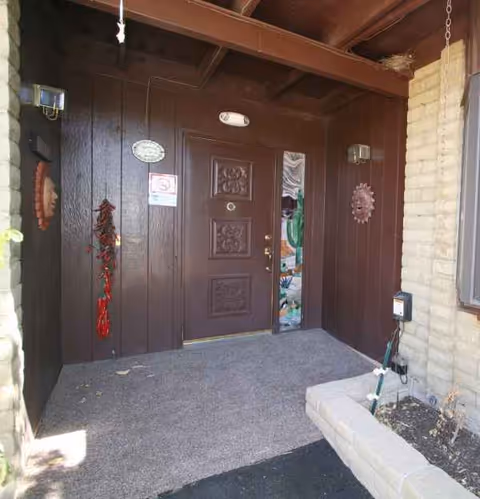 Dark brown wooden front door with decorative panels, flanked by brick walls and a small porch.