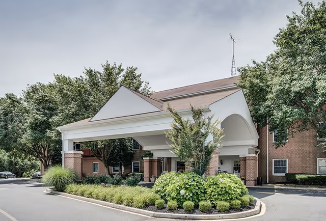 Covered entrance canopy and circular driveway with landscaping in front of a brick senior living building.