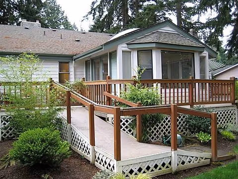 Exterior view of a single-story senior living home with a wooden deck and greenery.