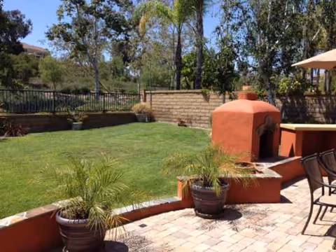 Outdoor patio with potted plants, brick seating area, an oven/fireplace, umbrella, and lawn