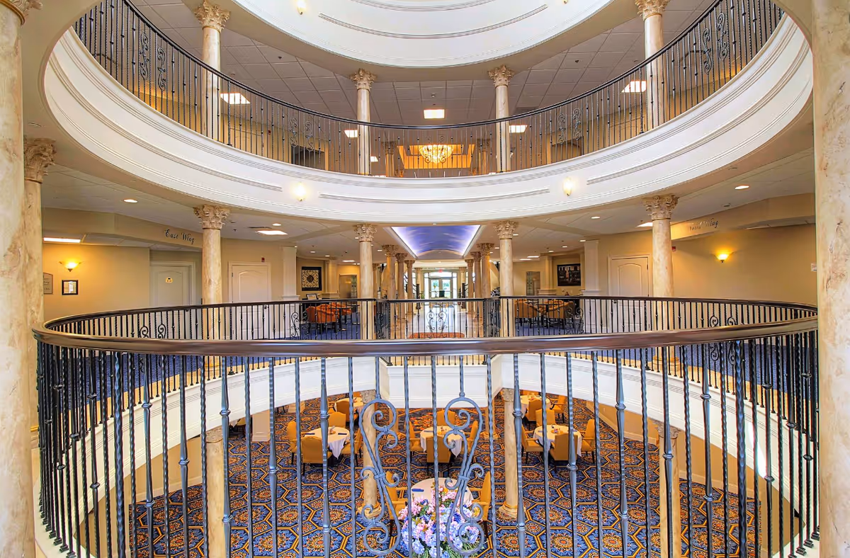 Multi-level interior atrium with circular balconies, ornate railings and columns overlooking seating and dining tables below.