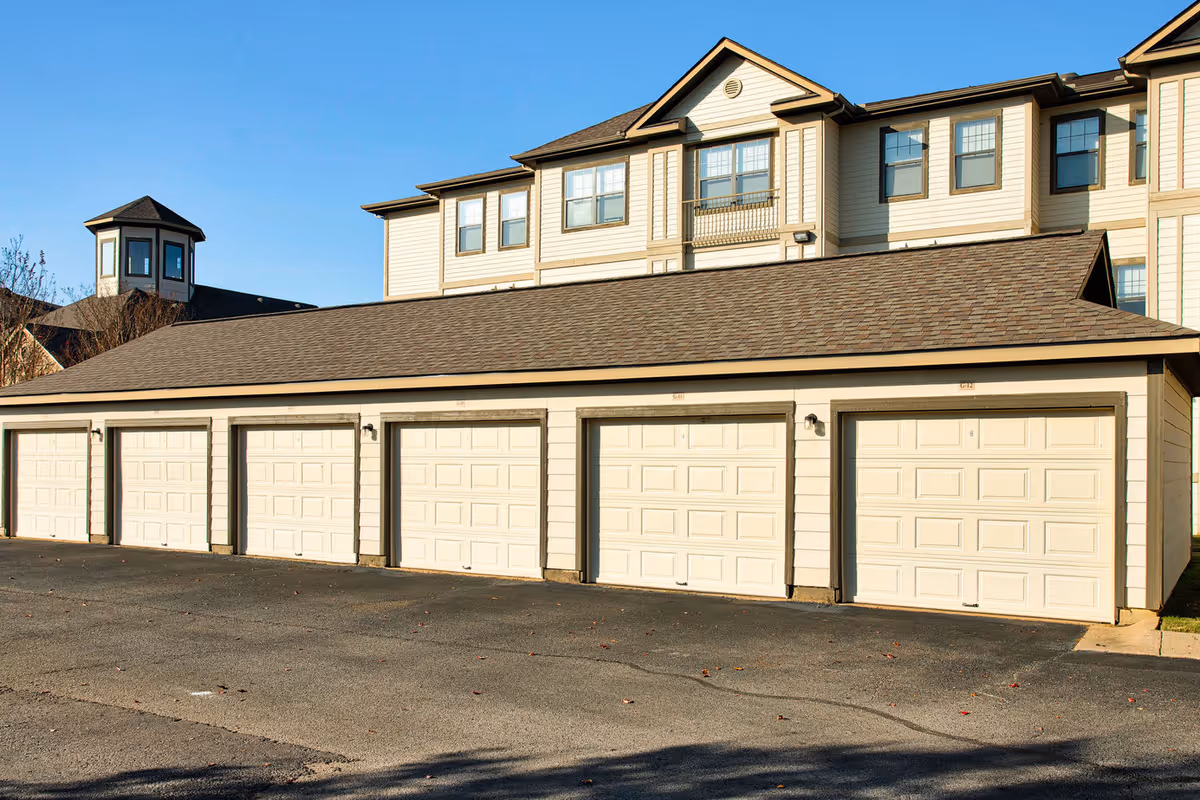 A row of attached garage doors in front of a multi-story residential building under a clear blue sky.