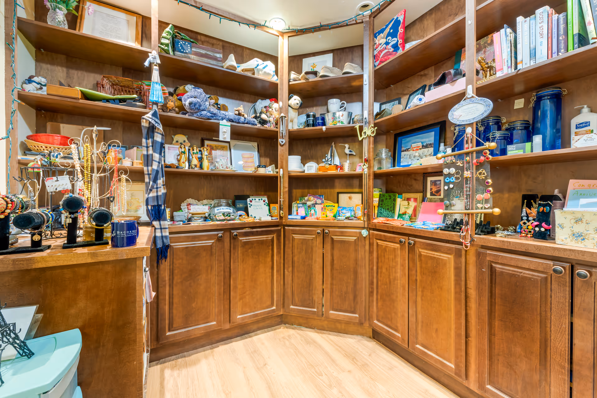 Wood-paneled interior shelving and cabinets displaying a variety of small gifts, jewelry, and decorative items in a boutique-like shop area.